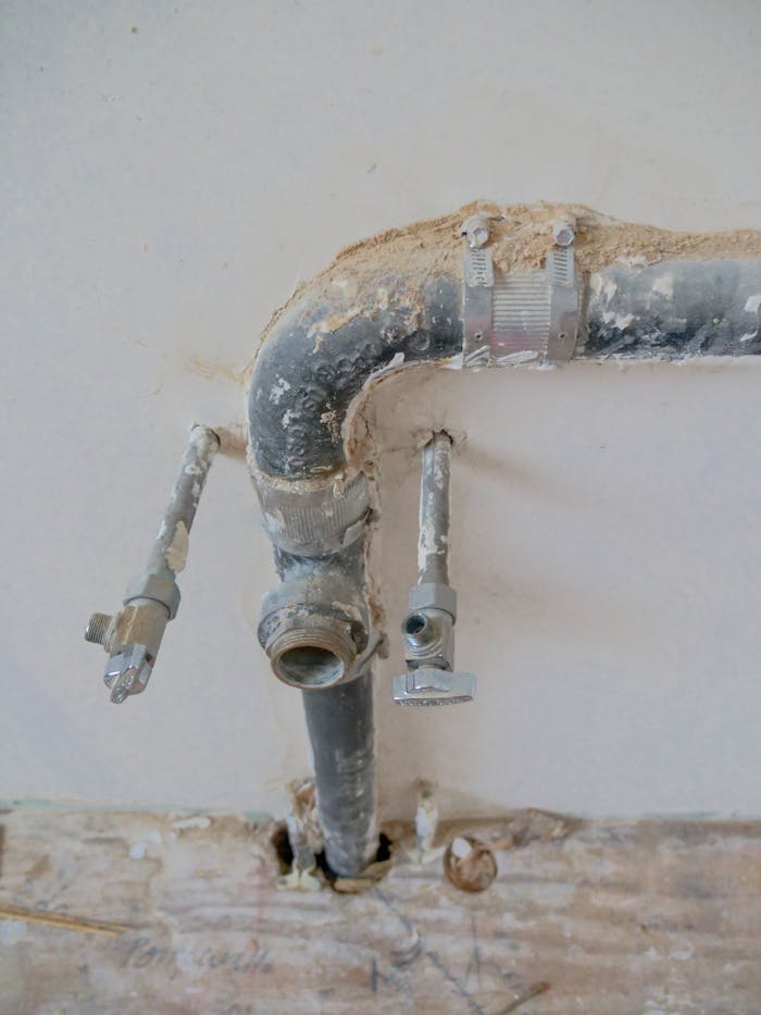 Close-up of exposed plumbing pipes with rustic textures on a construction site wall.